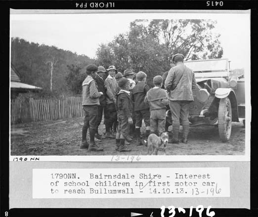 black and white photo of a man showing children a motor car