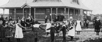 Black and white photo, children playing outside of a school